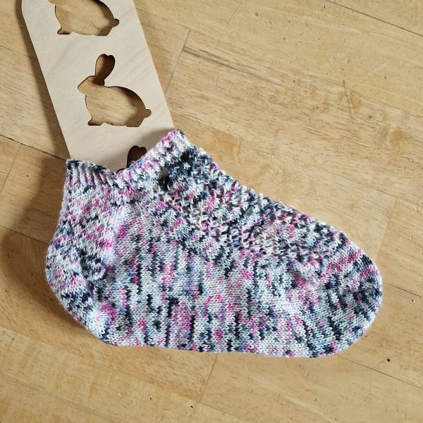 A sock with three panels of lace on the foot, knit in speckled white, black and pink yarn