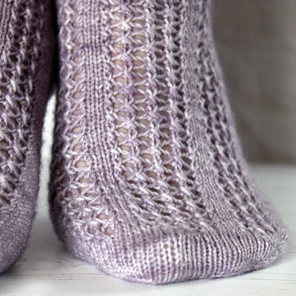 A close up on the toe of modelled socks with three panels of lace on the foot, knit in purple yarn