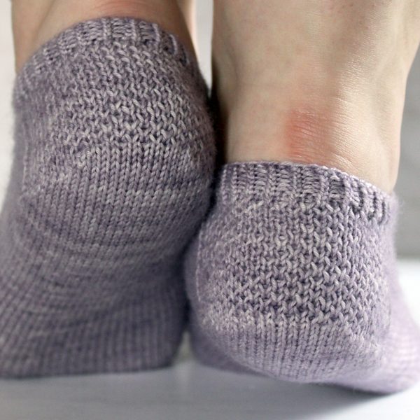 A close up on the textured heels of modelled socks with three panels of lace on the foot, knit in purple yarn