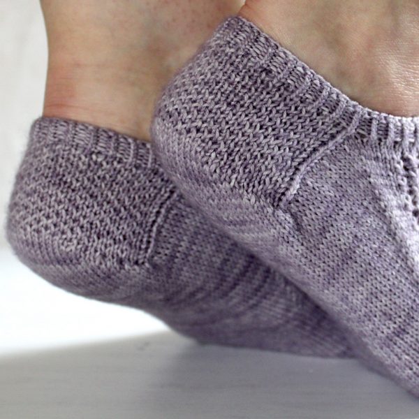 A close up on the textured heels of modelled socks with three panels of lace on the foot, knit in purple yarn