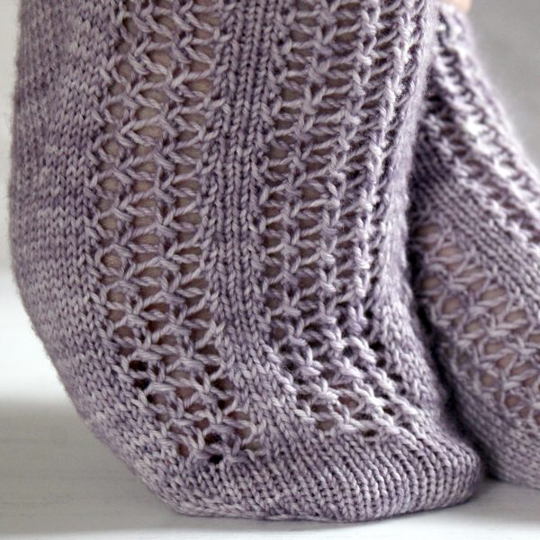 A close up on the toe of modelled socks with three panels of lace on the foot, knit in purple yarn