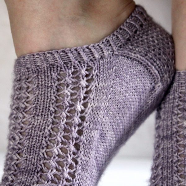 A close up on the heel and cuff of modelled socks with three panels of lace on the foot, knit in purple yarn