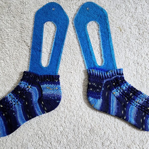 A pair of socks with three panels of lace on the foot, knit in striped blue yarn