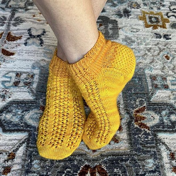 A pair of modelled socks with three panels of lace on the foot, knit in yellow yarn