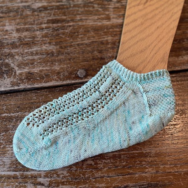 A sock with three panels of lace on the foot, knit in pale blue yarn