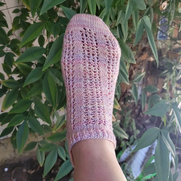 A of modelled sock with three panels of lace on the foot, knit in pink yarn