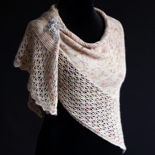 A shawl with an arrow shaped lace border and garter stitch body of a shawl knit in pale yellow speckled yarn and draped around a mannequin with a silver shawl pin on the shoulder