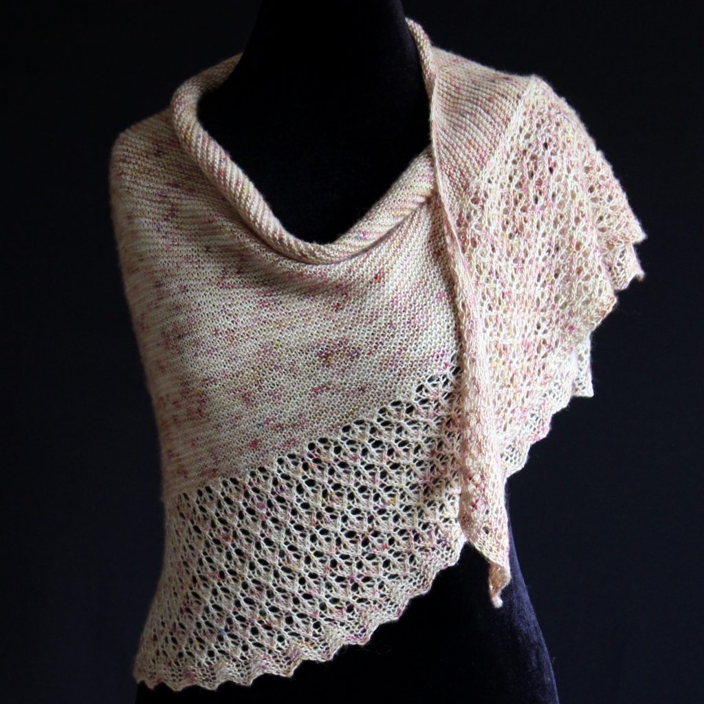 A shawl with an arrow shaped lace border and garter stitch body of a shawl knit in pale yellow speckled yarn and draped around a mannequin