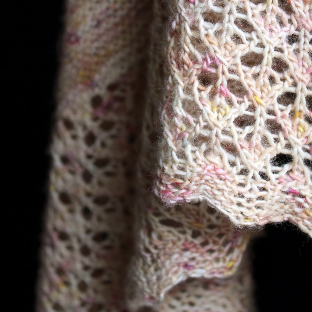 A close up on a the lace border of a shawl with garter stitch knit in pale yellow speckled yarn