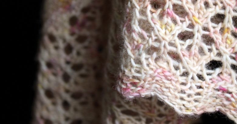 A close up on a the lace border of a shawl with garter stitch knit in pale yellow speckled yarn