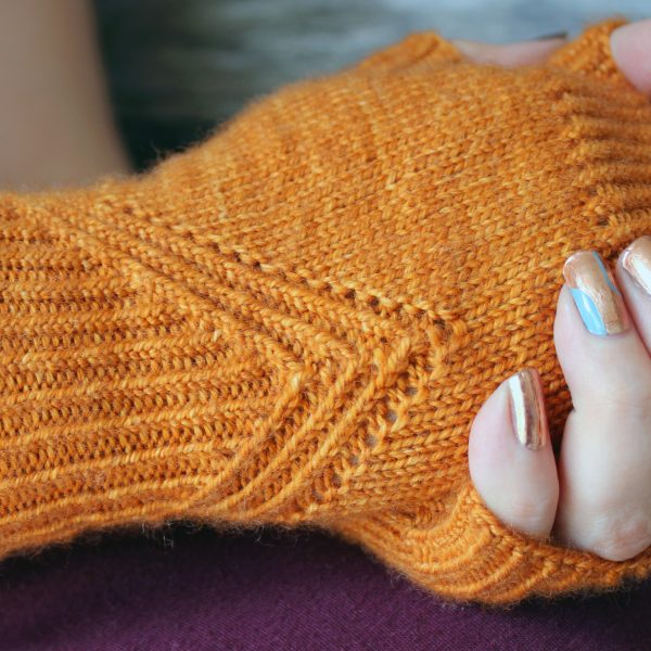 Fingerless mitts in orange yarn with a twisted rib pattern that decreases to a point below the ring finger.