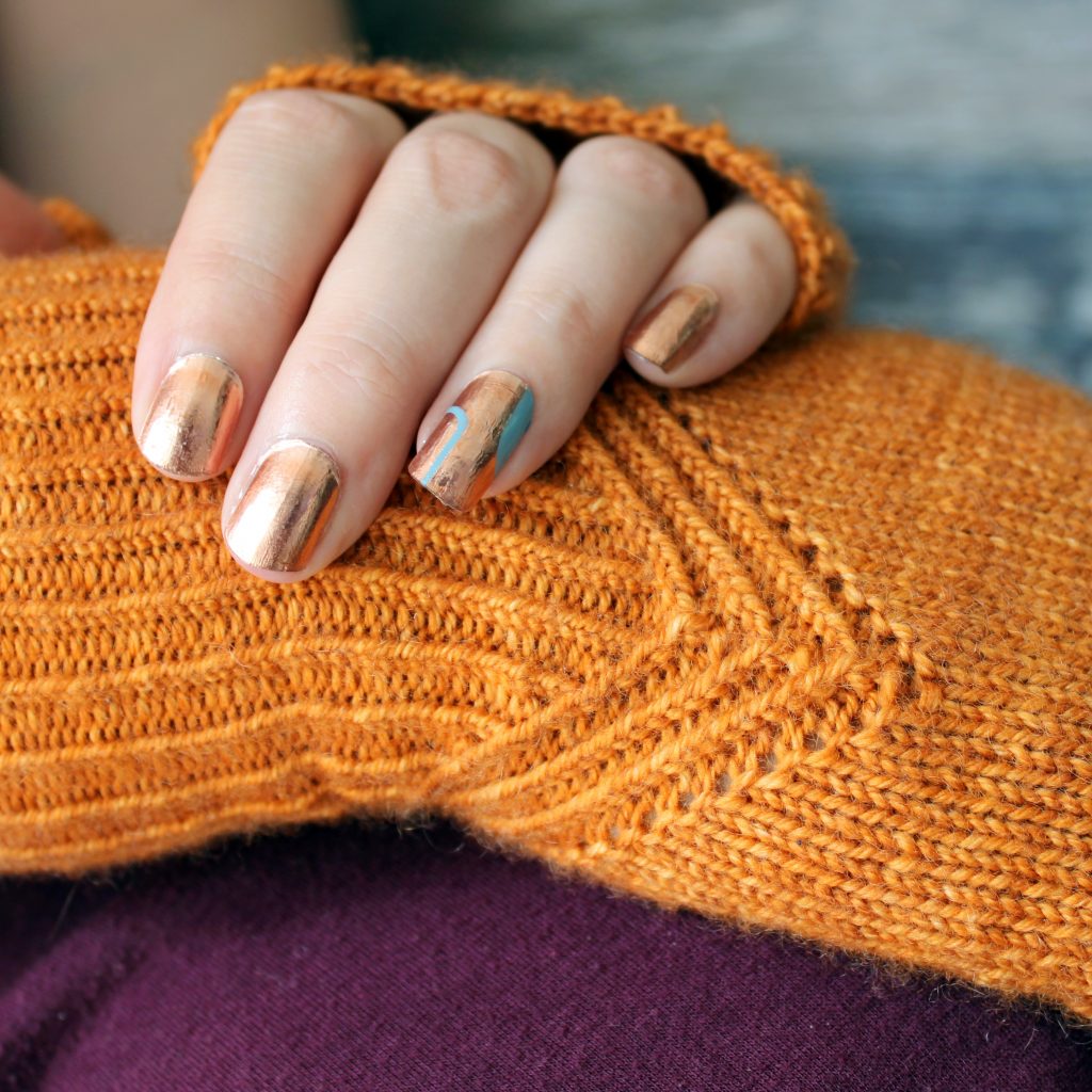 Fingerless mitts in orange yarn with a twisted rib pattern that decreases to a point below the ring finger.