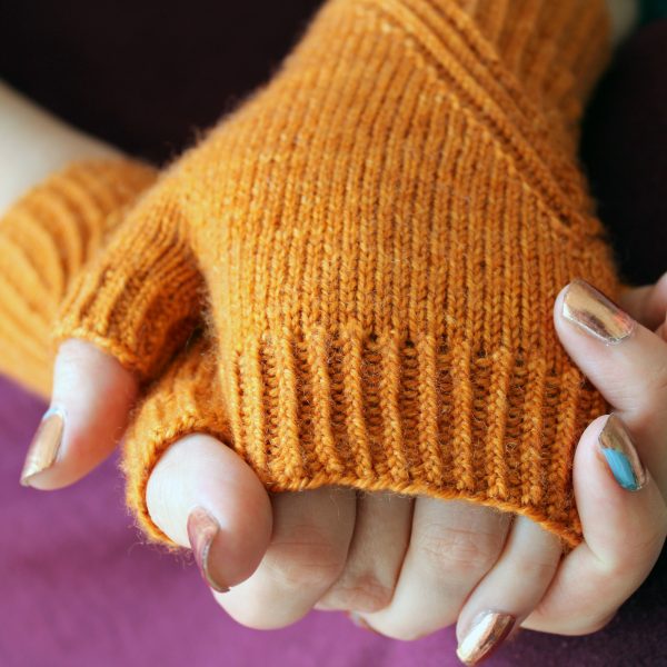 Fingerless mitts in orange yarn with a twisted rib pattern that decreases to a point below the ring finger.