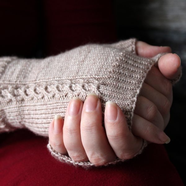 A pair of fingerless mitts with a twisted cable pattern, knit in a pale tan yarn