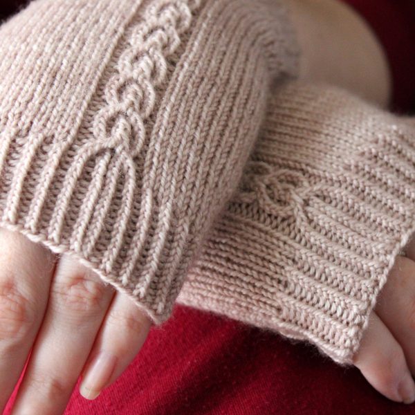 A close up on the cuffs of a pair of fingerless mitts with a twisted cable pattern, knit in a pale tan yarn