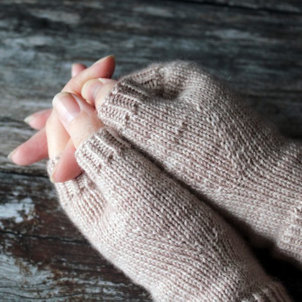 The thumbs of a pair of fingerless mitts, knit in a pale tan yarn